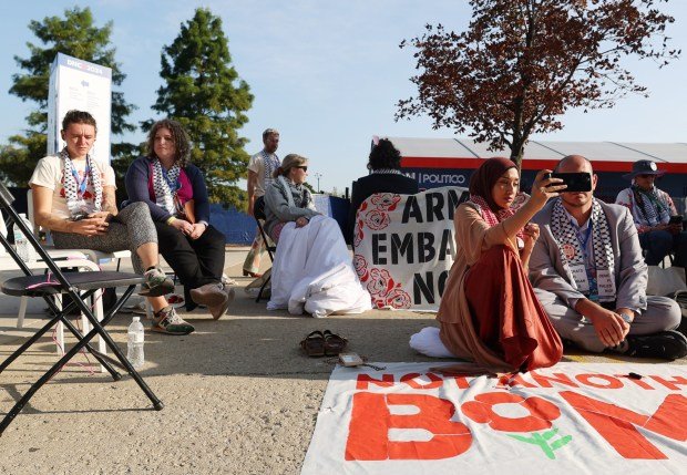 Taahhüt vermeyen delegeler ve 'Takım' üyeleri, Filistinli bir Amerikalının konuşma hakkı almasını talep etmek için DNC'de oturma eylemi yaptı 1 Uncommitted delegates sit on the ground Asma Nizami, left, and Abbas Alawieh, right, participate an interview on their phone with national media while during a sit-in in front of the United Center on Aug. 22. 2024, in Chicago. (Stacey Wescott/Chicago Tribune)