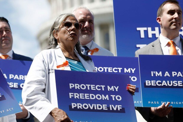 Tüp bebek tedavisine yönelik potansiyel tehditler, siyasette yeni olan kişileri seçim yılı savunuculuğuna itiyor 1 Protesters in medical coats hold blue signs that say "Protect My Freedom To Provide IVF"